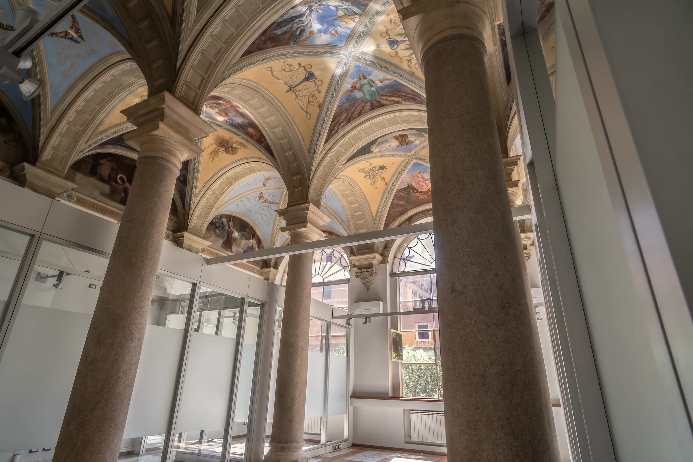 Vista dal basso di volte affrescate e colonne in granito, con le pareti divisorie in vetro che si fermano prima del soffitto