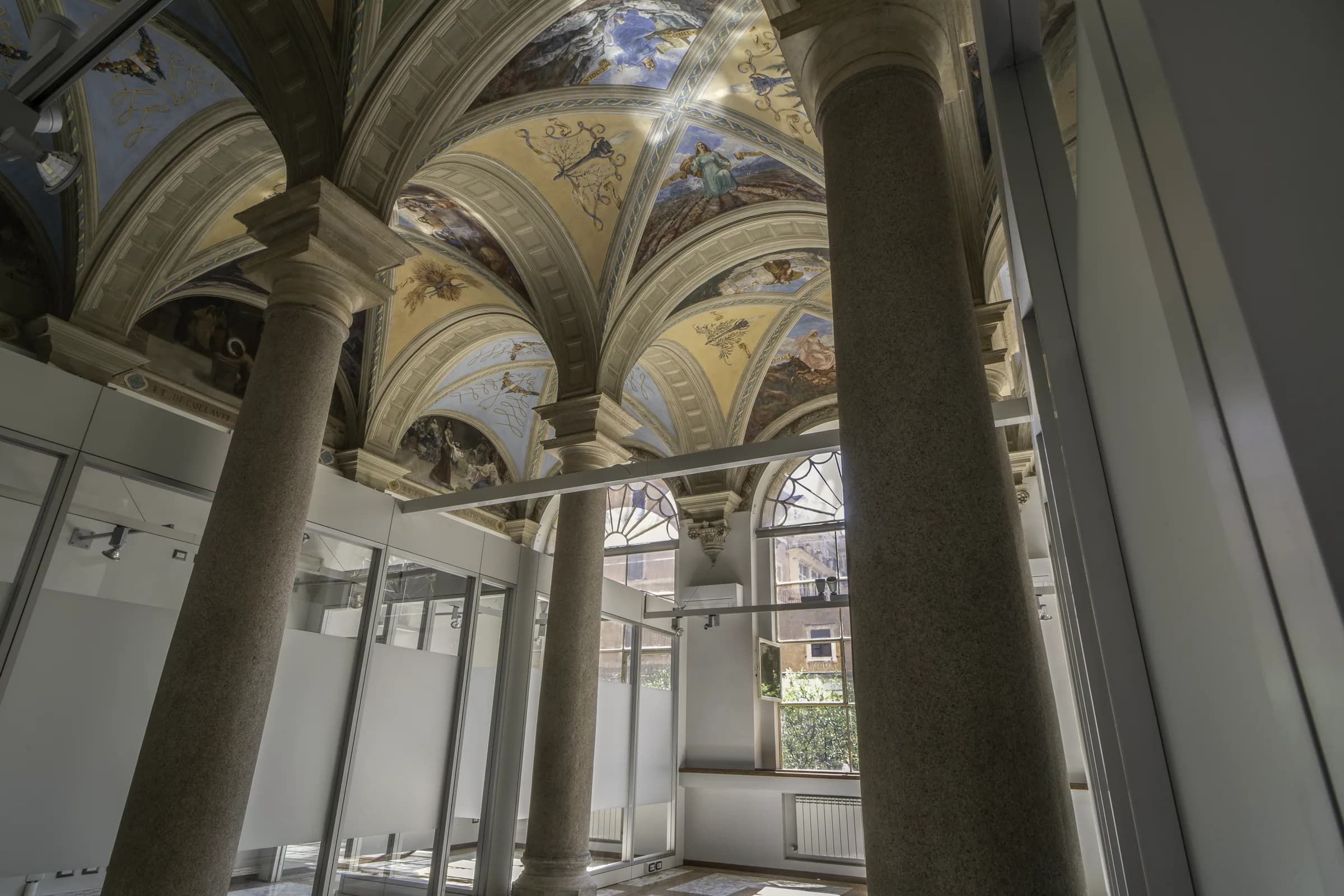 Vista dal basso di volte affrescate e colonne in granito, con le pareti divisorie in vetro che si fermano prima del soffitto