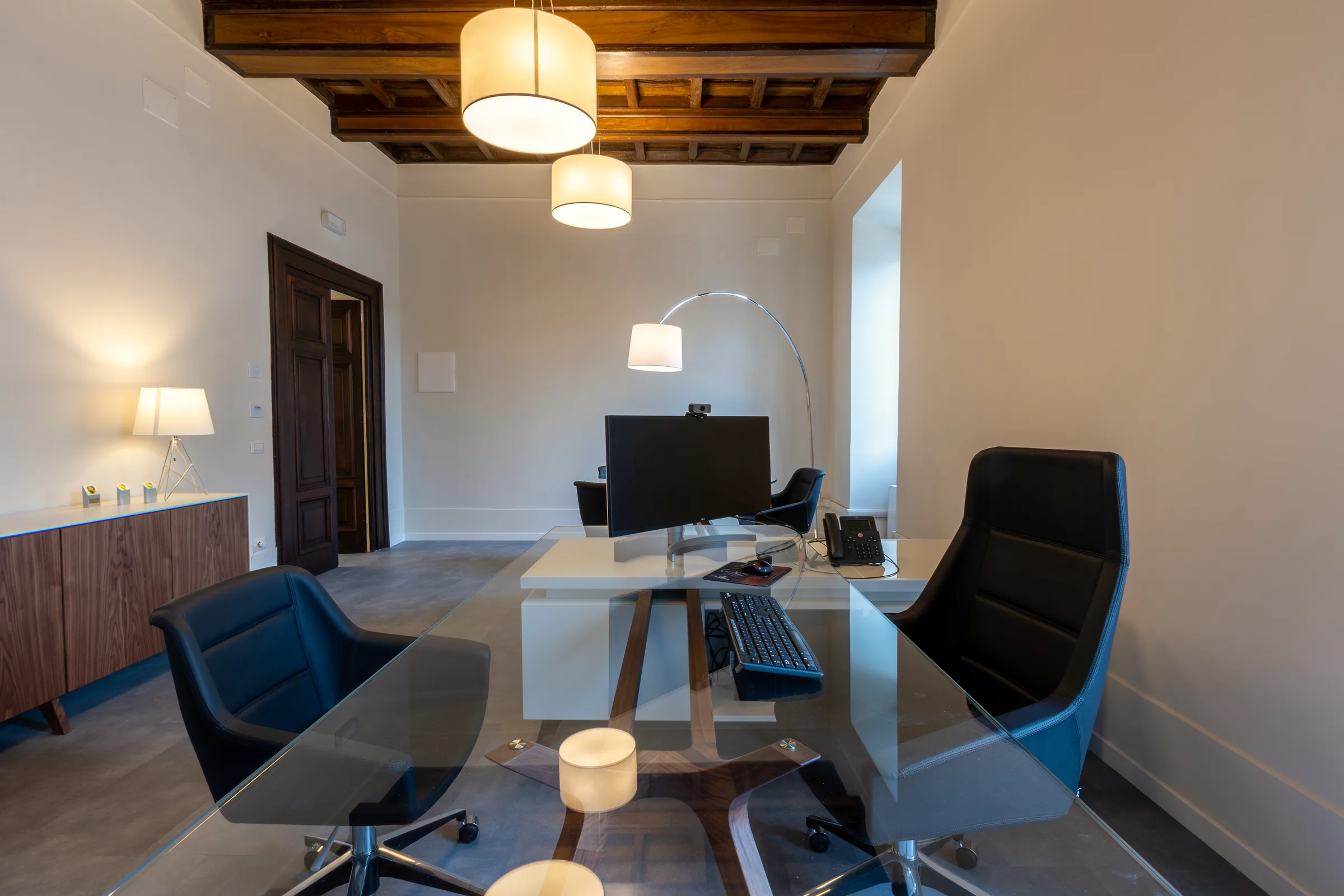 Ufficio luminoso con scrivania, sedute verdi, area conversazione e ampie finestre schermate da tende avvolgibili.